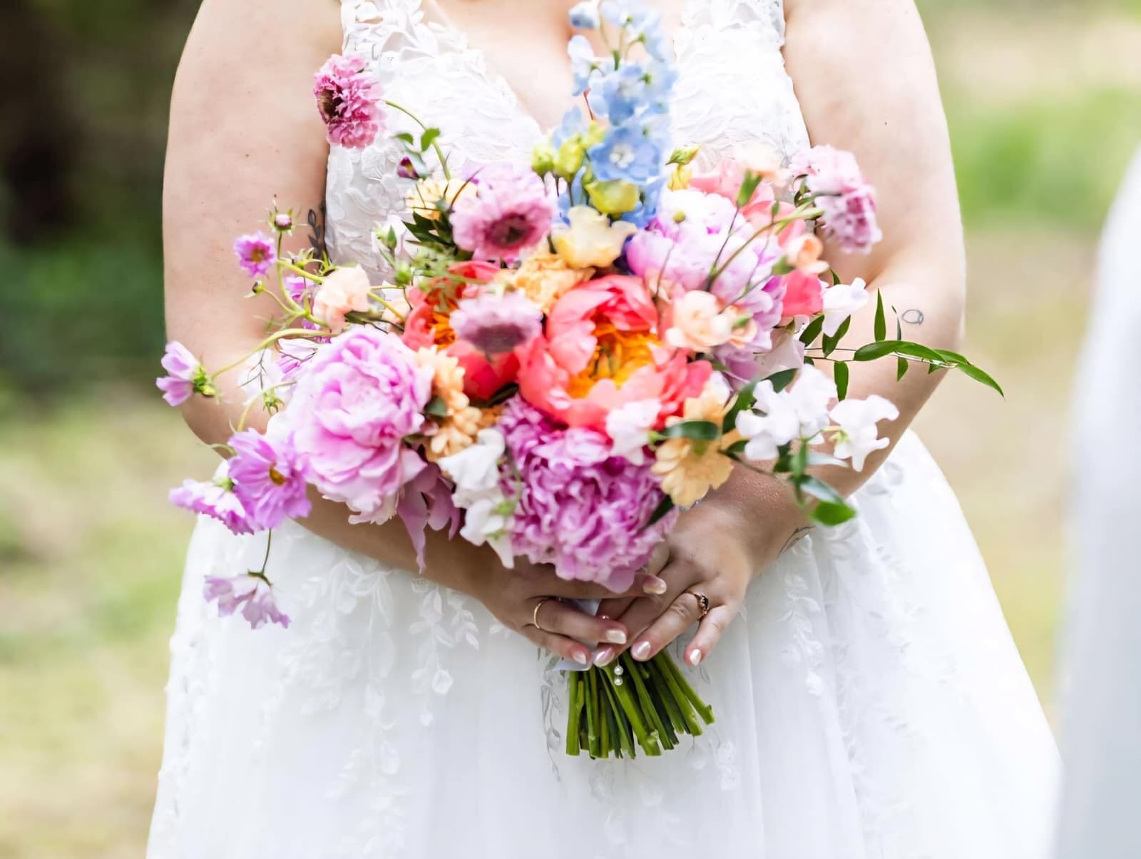 Brud med farverig brudebuket af pæoner og ærteblomster
