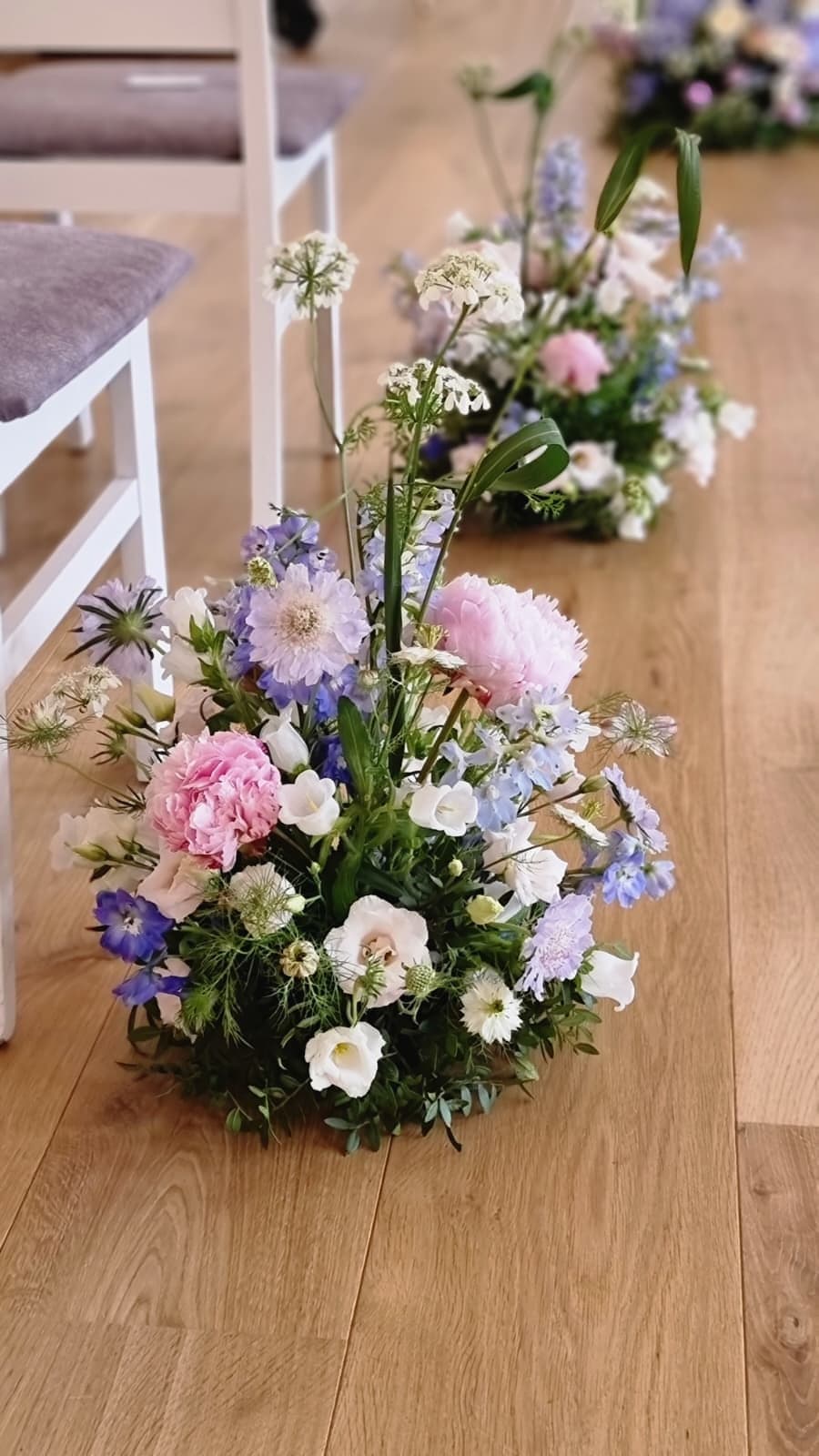 Gulvdekorationer med pæoner, ridderspore og scabiosa langs en ceremonigang